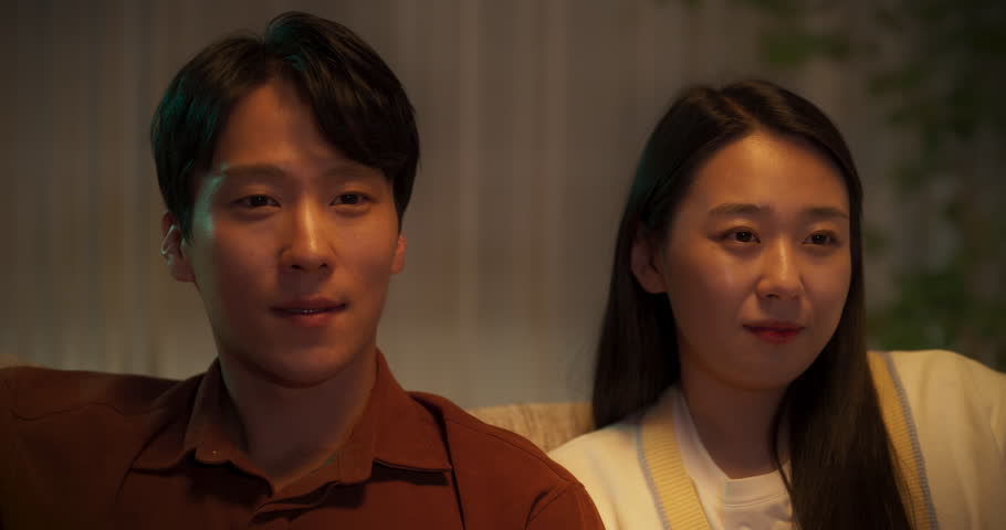 Young Asian Couple Watching a Movie on an Online Streaming Service while Sitting on a Couch at Home. South Korean Man and Beautiful Girlfriend Spending Time Together and Enjoying a Romantic TV Show Royalty-Free Stock Footage #1105013773