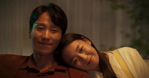 Young Asian Couple Watching a Movie on an Online Streaming Service while Sitting on a Couch at Home. South Korean Man and Beautiful Girlfriend Spending Time Together and Enjoying a Romantic TV Show วิดีโอสต็อก