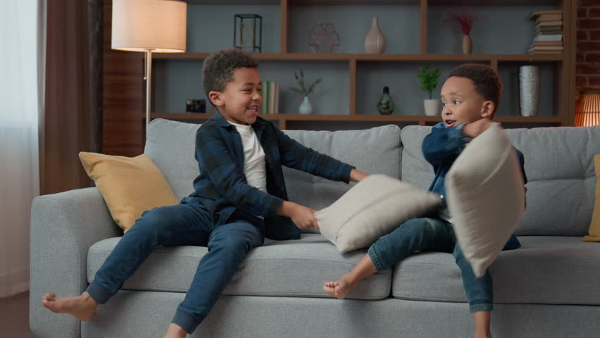 Two naughty little boys children fighting with pillows African American siblings brothers ethnic kids having fun playing fight battle play game fooling around at home living room couch ADHD behavior Royalty-Free Stock Footage #1105014211