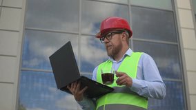 a man with a beard at a construction site drinks coffee. a man works at a laptop. slow motion video. High quality Full HD video recording