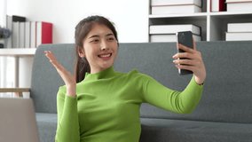 Pretty Asian woman sit on sofa at home enjoy with video call meeting with friend. Woman making content by smartphone at home
