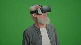 Green Screen. An Old Man With Gray Beard in VR Glasses Examines Everything Around. Virtual Reality Education for the Elderly.
