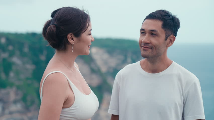 Asian man and woman they look at each other smiling and talk. Enthusiastic emotional happy Korean couple. Travel moments for happy family on a wild seaside on summer holiday. Vacation on ocean shore Royalty-Free Stock Footage #1105023103