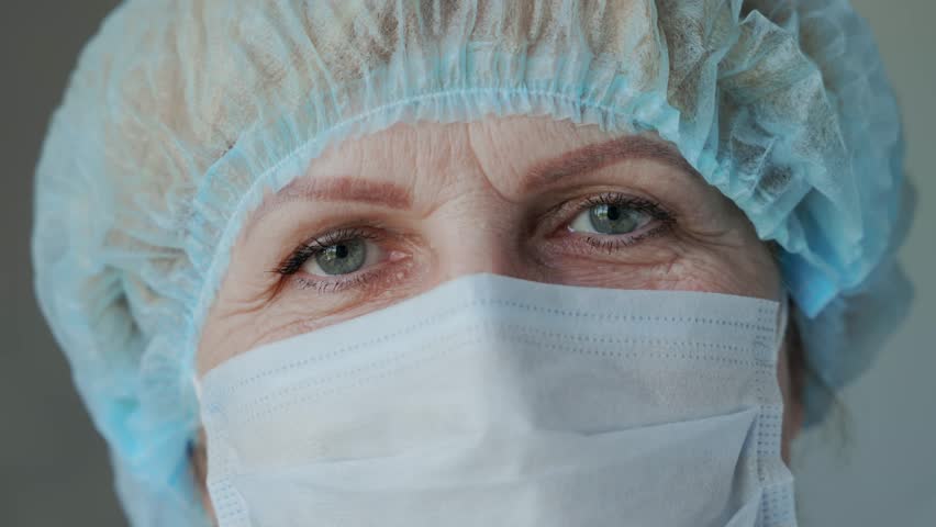 Close-up portrait of the face of an elderly woman with wrinkles in a medical mask and cap. An old doctor, tired of his job. Work in the quarantine zone. High quality 4k footage Royalty-Free Stock Footage #1105032069