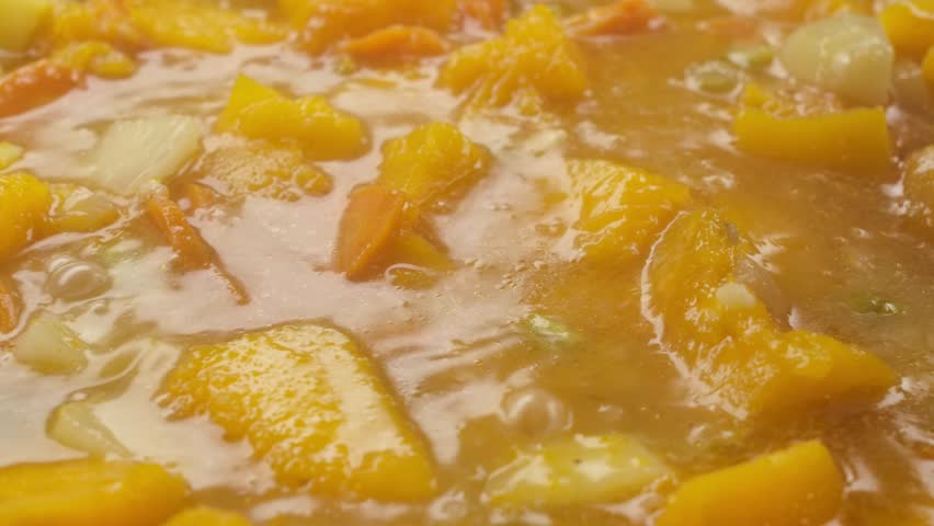 Close-up of the pumpkin soup boiling with the vegetables n the pan in slow motion