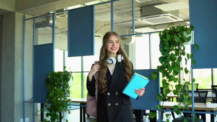 Happy student girl says yes, passed an important test, raises hand with fist in excitement, smiles sincerely, throws backpack, holding books, wearing white t-shirt and suite, and headphones over neck Royalty-Free Stock Footage #1105033611