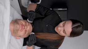 Vertical video. A beautician wipes the face of a client's boy with a cotton sponge in a beauty salon