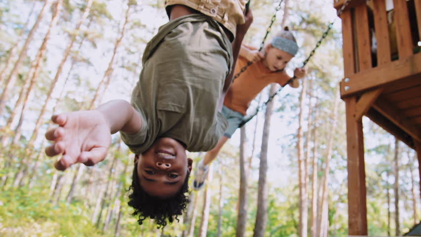 Medium tracking shot of African American elementary age boy hanging upside down on playground at daytime Royalty-Free Stock Footage #1105041393