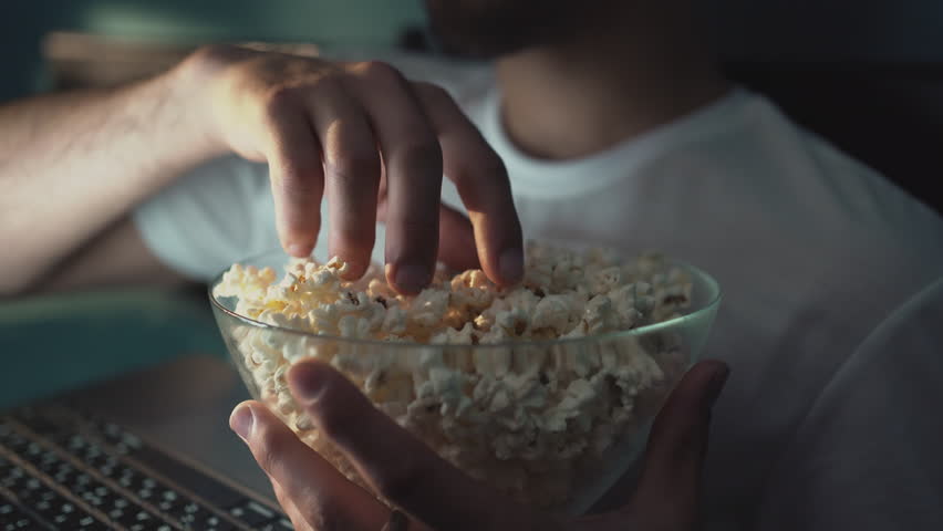 Single man watching online tv in the night sitting on a bed in the bedroom at home. Eating popcorn. Royalty-Free Stock Footage #1105042559