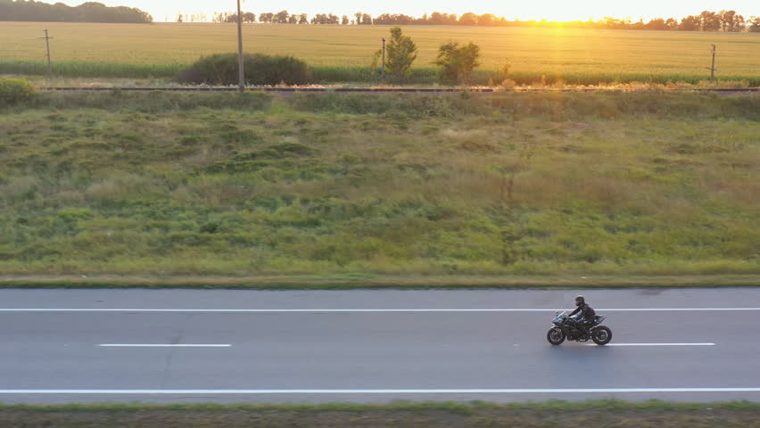 Motorcyclist racing his motorcycle on country road. Man in helmet rides on modern sport motorbike at highway with sun at background. Guy driving bike during trip. Concept of freedom. Aerial view Royalty-Free Stock Footage #1105043111