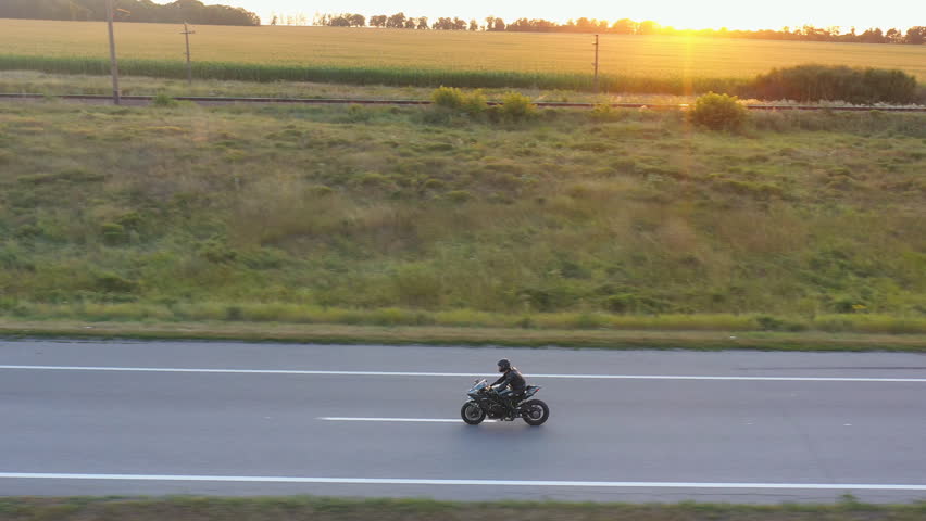 Motorcyclist racing his motorcycle on country road. Man in helmet rides on modern sport motorbike at highway with sun at background. Guy driving bike during trip. Concept of freedom. Aerial view