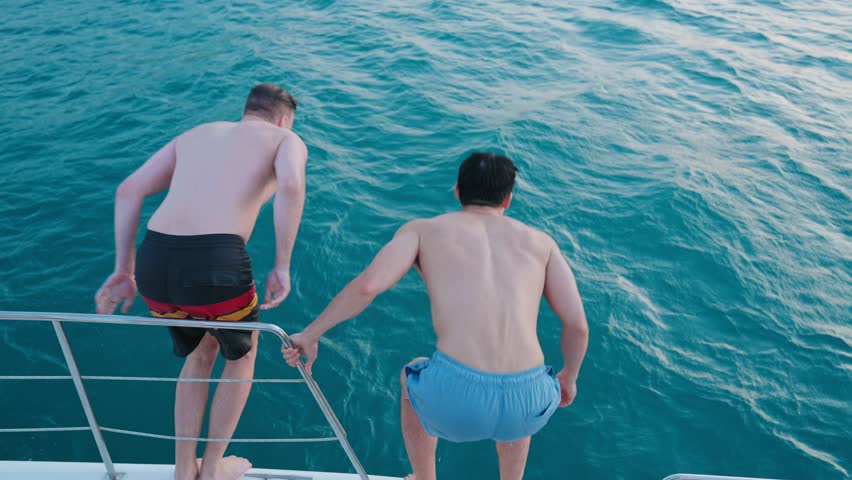 Group of diverse people having fun jumping in the sea water from the yacht during summer. Friends in swimming costume hopping at boat ladder of yacht while yachting in sunny day. Friendship concept Royalty-Free Stock Footage #1105043521