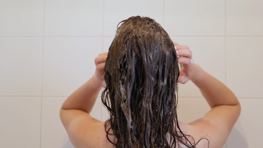 A woman washes her long, dark hair with shampoo. Female Wash Brunette Hair On Head With Shampoo In Shower. Concept of hair care and personal hygiene. Back view. Slow motion. Royalty-Free Stock Footage #1105049405