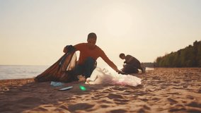 Volunteers guys collecting trash garbage and sorting in bags on ocean coast at sunset. Environment pollution protection. Put on trash, rubbish, waste, junk in plastic pockets,volunteering. Blur video.