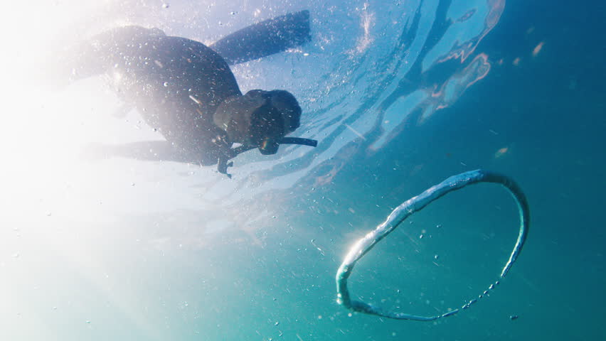 Free diver swims underwater in the murky sea and glides through the ring bubble. Freediver plays underwater with ring bubble Royalty-Free Stock Footage #1105059915