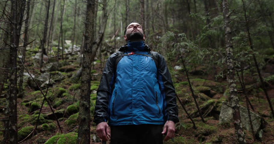 Portrait of a man with a backpack standing in the rain in the forest and raising his hands to the mountain breathing in the mountain air and meditating. The man is alone in the mountains. Hiking among