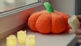 tabby cat sitting on window sill with soft toy pumpkin or on blanket with halloween candle.spooky holiday.girl woman hands lighting plastic candles putting on sill.  owner petting animal - Powered by Shutterstock - Get 15% off with code: PIKWIZARD15