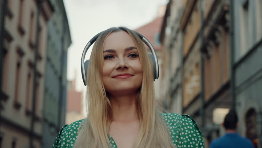 Gimbal portrait of happy blond hair woman wearing green dress walks through busy narrow street listening music with headphones enjoying summer evening and architecture in historical part of old town Royalty-Free Stock Footage #1105071453
