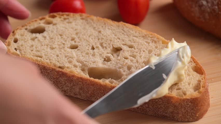 Woman spreading soft butter on slice of bread. Spreading cream cheese on bread. Housewife making sandwich for breakfast. | Shutterstock HD Video #1105073069