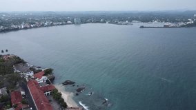 Aerial video on the beach of Sri Lanka. In the background a residential villagetown with the harbor, ships and green trees