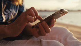 Close-up macro footage of aged female hands holding cell phone and texting message social media against golden light on sunset at seaside. Elderly lady tapping screen of mobile phone. Leisure outdoors - Powered by Shutterstock - Get 15% off with code: PIKWIZARD15