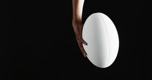 Vertical video of hand of african american man holding white rugby ball on black background. Rugby, sport, international, competition and games digitally generated image.