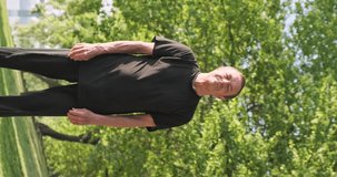 Caucasian man does qigong exercises, raises his hands up and slowly lowers them down, vertical video. Five beast games. City park, outdoors, wide angle.