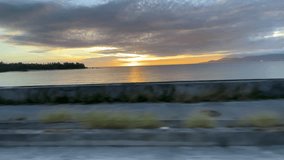 OKINAWA, JAPAN - JUNE 2021 : Driving at Nago city area in sunset time. Wide camera, point of view (POV), seaside road driving shot. Summer holiday, vacation and travel concept 4K video.