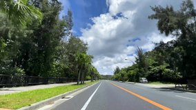 OKINAWA, JAPAN - AUG 2021 : Driving shot of Okinawa in daytime. Wide camera, point of view, seaside road drive. Blue sunny sky. Summer holiday, vacation and adventure journey travel concept 4K video.
