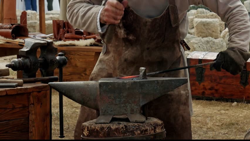 medieval historical reenactment - blacksmith forges metal by beating iron on the anvil in a medieval field during a fair