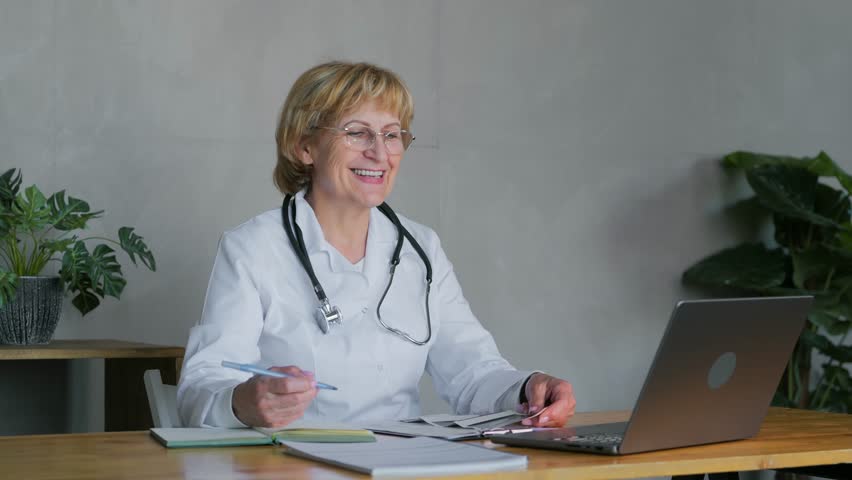 An adult female doctor is in the office and communicates with the patient on a video call using a laptop. Online consultation with a doctor. Medical support for patients online. High quality 4k Royalty-Free Stock Footage #1105094035