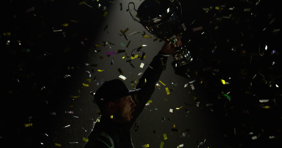 Silhouette of race car driver celebrating the win in a race against bright stadium lights, rising a trophy over his head Royalty-Free Stock Footage #1105099847