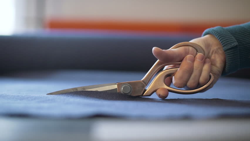 Hand holding big scissors and making cut of tissue. Probably it is tailor, designer, stylist or dressmaker making clothes in his or her studio. Close up shot.