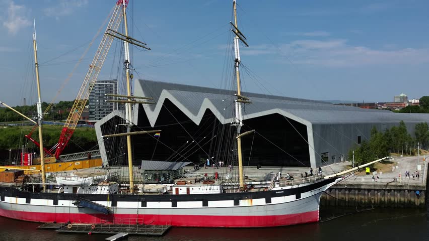 4K aerial panoramic outdoor drone video of riverside museum and tall ship at Glasgow harbour (Glenlee) taken on a sunny summer day in June 2023 in Glasgow, Scotland. River Clyde and people walking by.