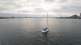 Drone aerial shot tracking a sail boat vessel in the San Diego Bay near the Pacific Ocean with the city skyline and downtown district in the background