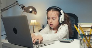 Portrait of Little Girl in Headphones with Laptop, Studying Online at Home, Interested Happy Student Typing on Keyboard, Looking at Computer Screen, Watching Webinar, Online Course, Doing Homework