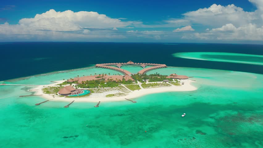 Water Villas Bungalows and wooden bridge at Tropical beach in the Maldives at summer day. Aerial drone view 4K.