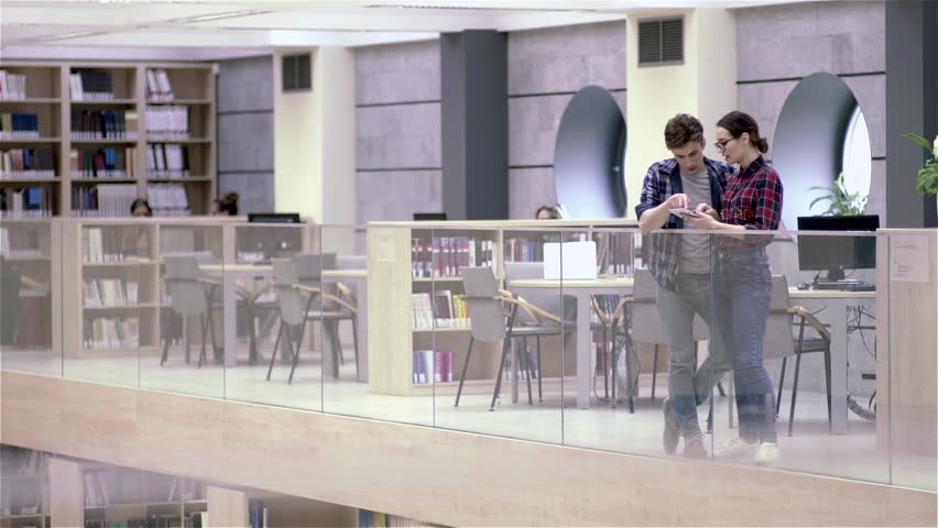 Two young, attractive, cheerful and friendly youth people are talking to each other in corporate background (company office or university library).