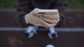 Cute girl in a sweatshirt with a smartphone in her hands on a street sports ground. close-up of female hands with a smartphone, outdoors. sunny warm day. shooting from the top. horizontal video