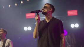 Close-up of man in black glasses performing song at concert into microphone. Live concert. Slow motion