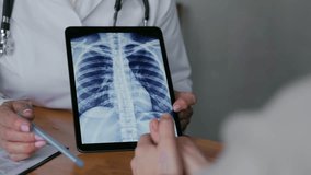 Consultation with a doctor. A close-up of a general practitioner shows the patient the results of an X-ray examination on an electronic tablet, pointing with a pen to the problem areas. 4k footage