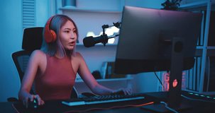Footage of Young Asian esport woman gamers playing online video games on the computer with neon light at home. Attractive girl gaming player feels enjoy technology broadcast live streaming.