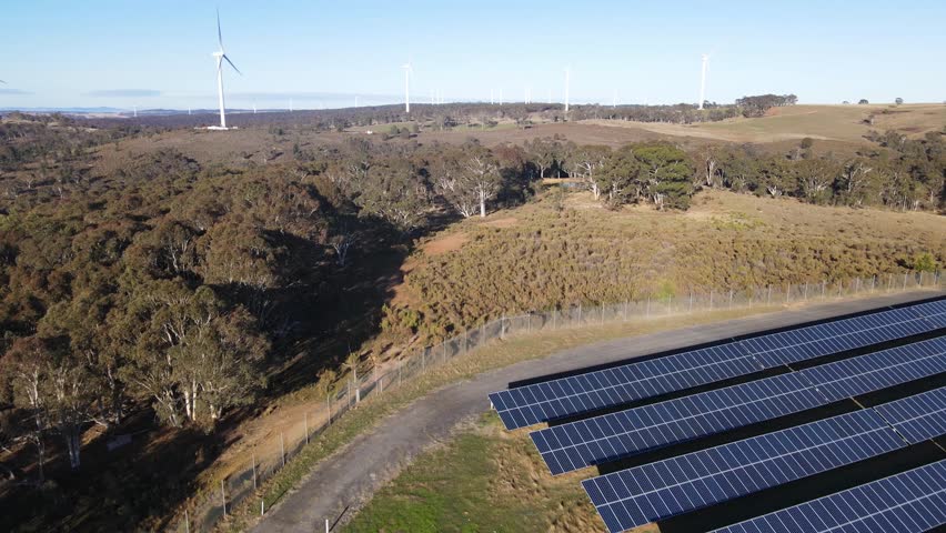 Aerial drone pullback reverse view of a hybrid wind and solar farm for renewable clean energy supply located at Bannister in the Upper Lachlan Shire, NSW, Australia on a sunny morning   Royalty-Free Stock Footage #1105118865