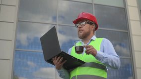a man at a construction site drinks coffee and holds a laptop in his hands. slow motion video. High quality Full HD video recording