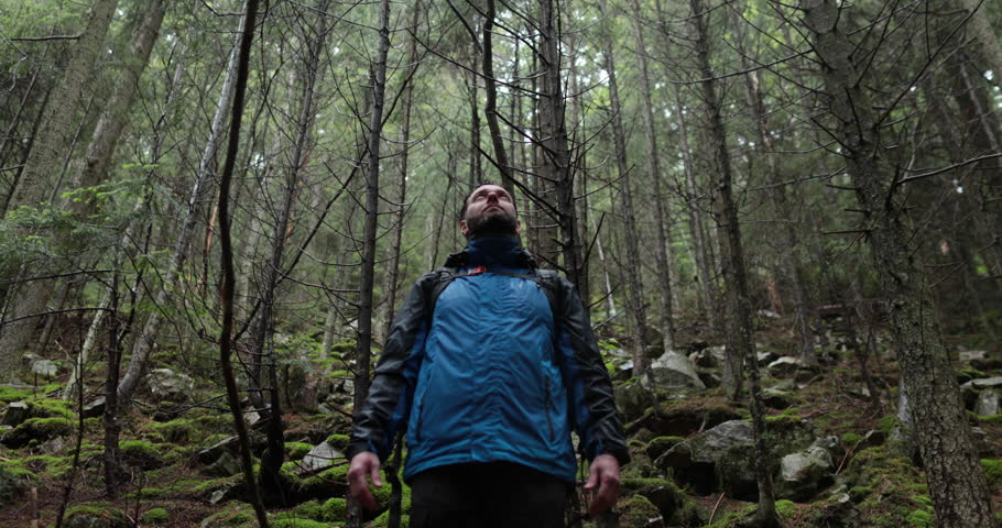 Portrait of a man with a backpack standing in the rain in the forest and raising his hands to the mountain breathing in the mountain air and meditating. The man is alone in the mountains. Hiking among