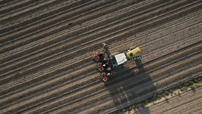 Aerial footage of farmer and agricultural workers in tractor and semi automatic planter planting tomato plants on harrowed land.