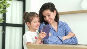 Cute funny little girl having fun with mom, enjoy using modern gadget, smart phone, looking at mobile phone screen, laughing, making conference call on app, watching social media videos