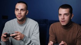 Happy Smiling friends with gamepads joystick controller playing video game on sofa at home. Portrait of caucasian guys playing game with console relaxing on couch at home.