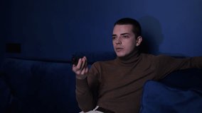 Young caucasian man relaxing on cozy couch, choosing online film movie, watching show entertaining programs, spending free weekend time alone on sofa at home.