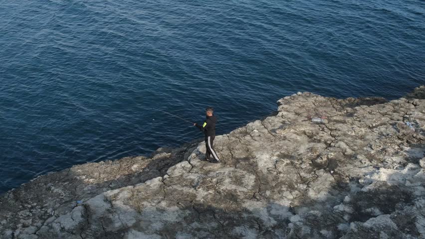 Young fisherman on seashore, boy on the cliffs by the sea, young man fishing on the cliff, image of the fishing from the sea using a rod